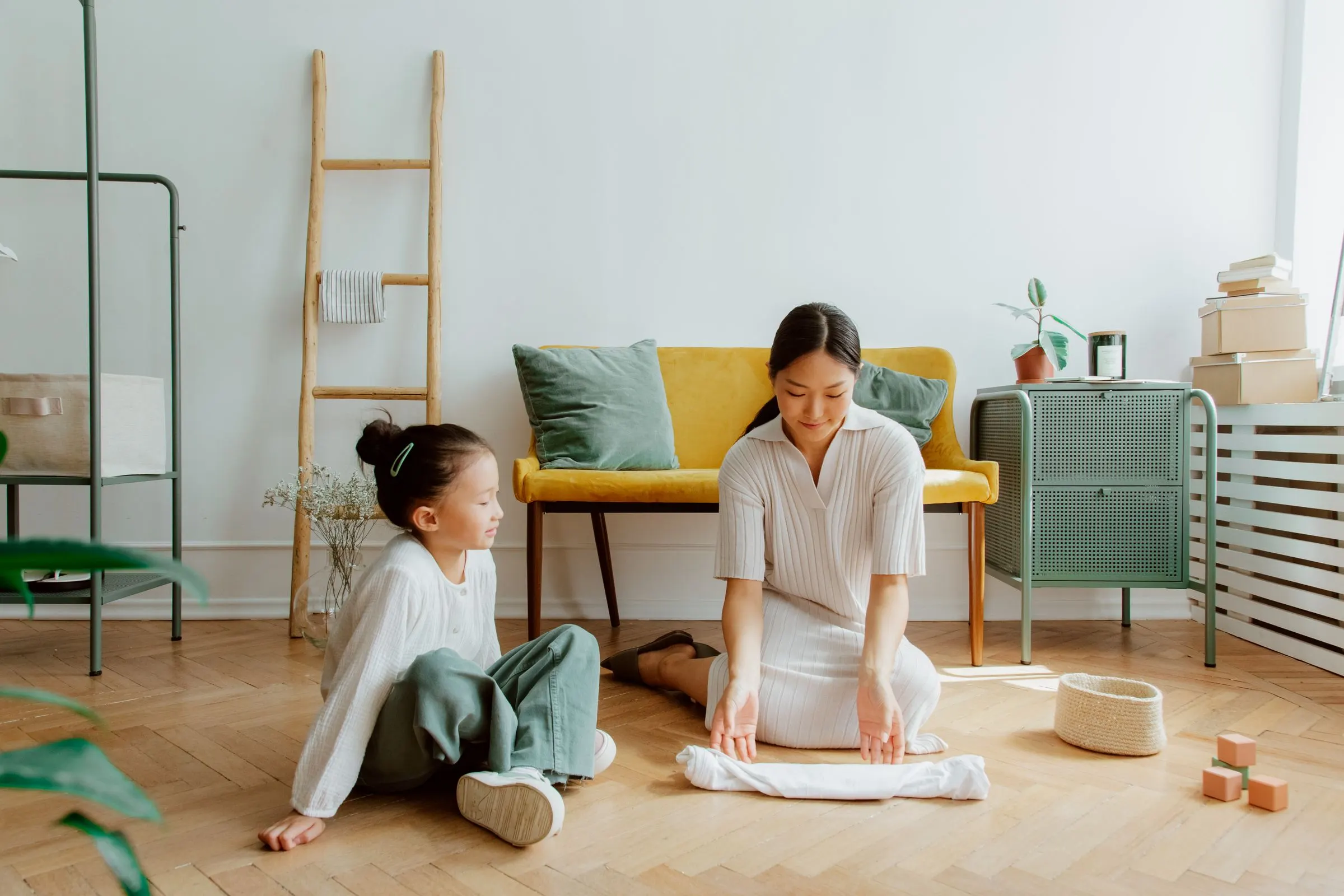 A mother and daughter folding a clean white towel together at home